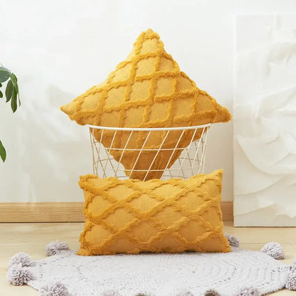 A mustard-yellow textured diamond cushion cover with embroidery and frayed edges displayed in a wire basket