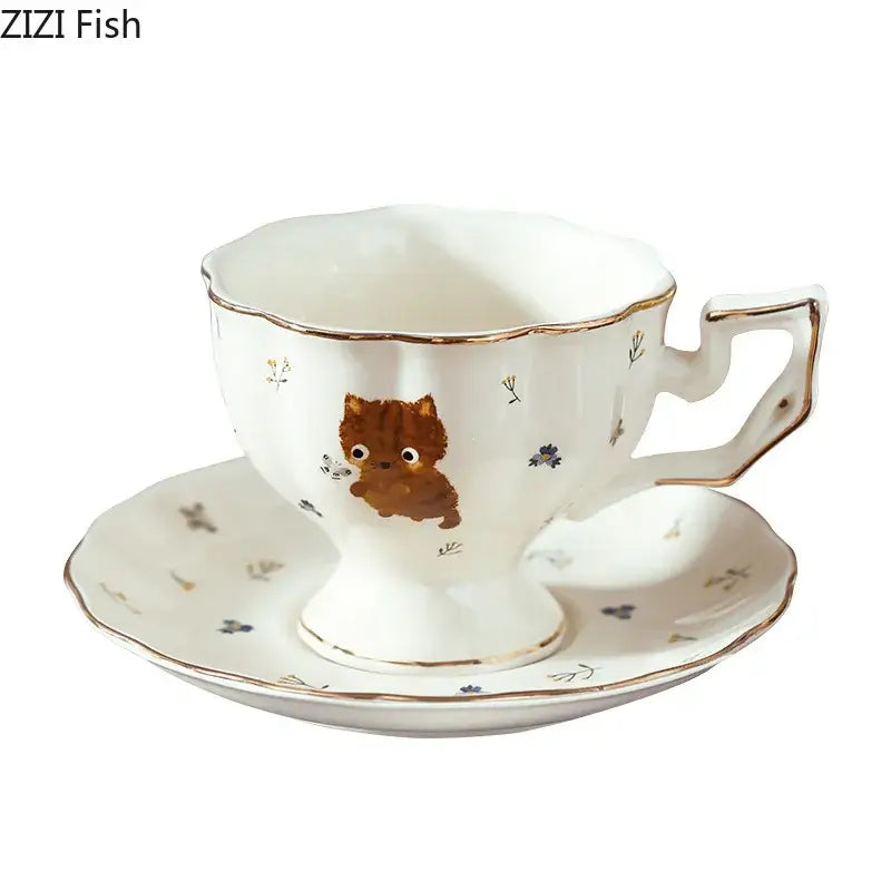 White ceramic teacup and saucer set with gold trim featuring a cartoon kitten pattern and tiny floral designs