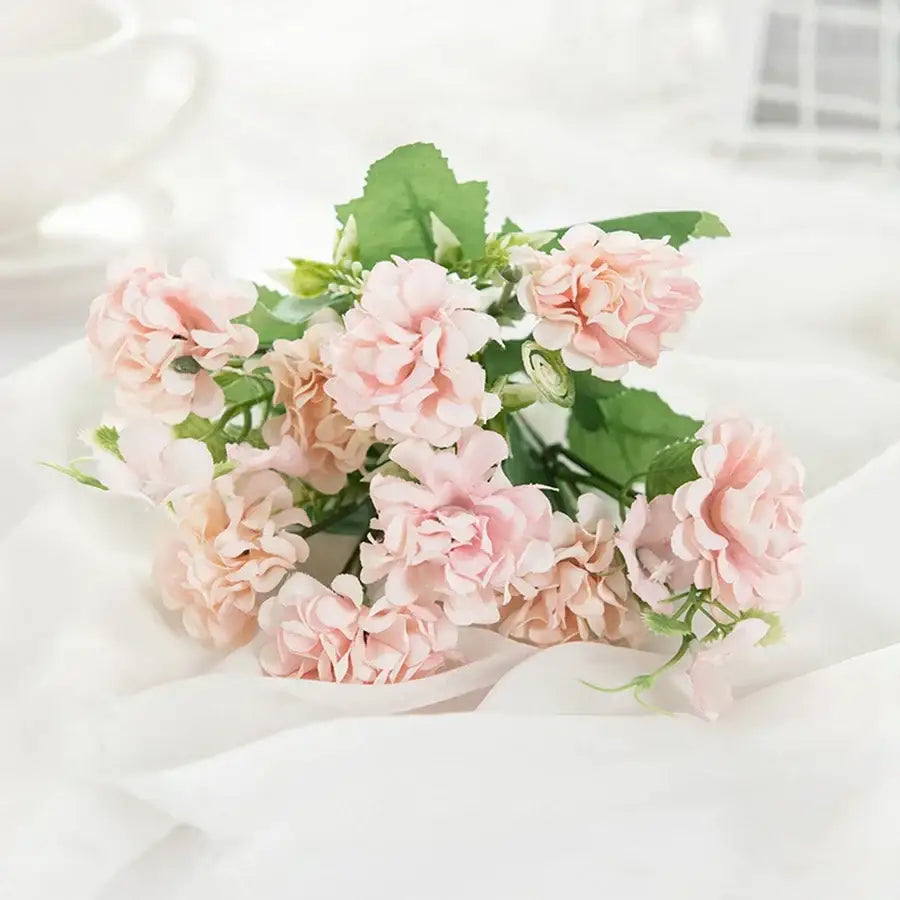 A delicate bouquet of soft pink artificial flowers with green leaves on white fabric for decorbites hydrangea bouquet