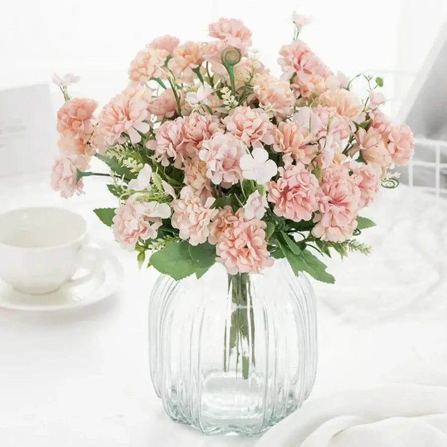A clear ribbed glass vase holding a soft pink and white decorbites hydrangea bouquet with green foliage for living room decor