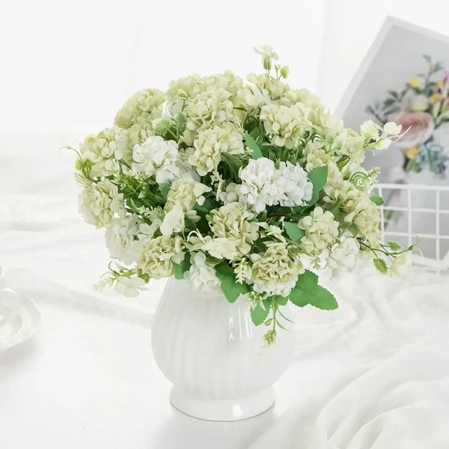 A decorbites hydrangea bouquet of artificial cream and white flowers with green foliage in a white ribbed glass vase