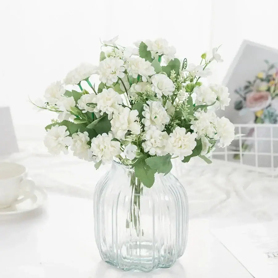 A clear ribbed glass vase with white artificial hydrangea bouquet and green leaves for living room decor by decorbites