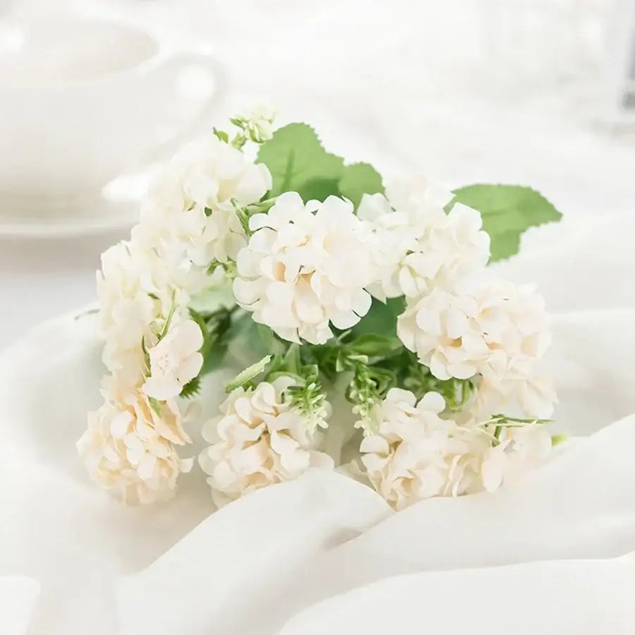 A delicate white hydrangea bouquet of artificial flowers with soft green leaves in a ribbed glass vase for decorbites decor