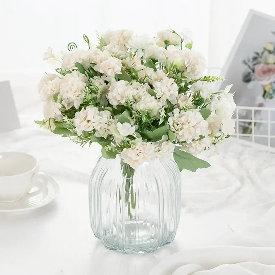 White hydrangea bouquet with green foliage in a clear ribbed glass vase for living room decor by decorbites hydrangea bouquet