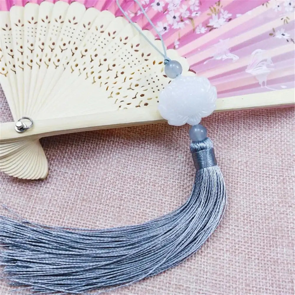 A delicate white jade lotus flower pendant with gray silk tassel and beads displayed on soft pink background