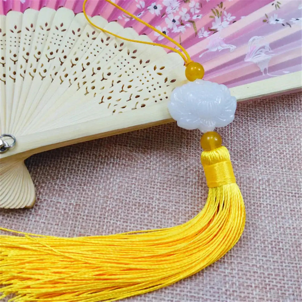 A delicate white jade lotus pendant with a golden bead and pink tassel for living room decor suspended from an ornate fan