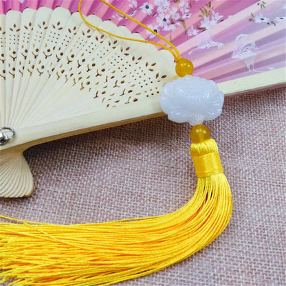 A delicate white jade lotus pendant with a golden bead and pink tassel for living room decor suspended from an ornate fan