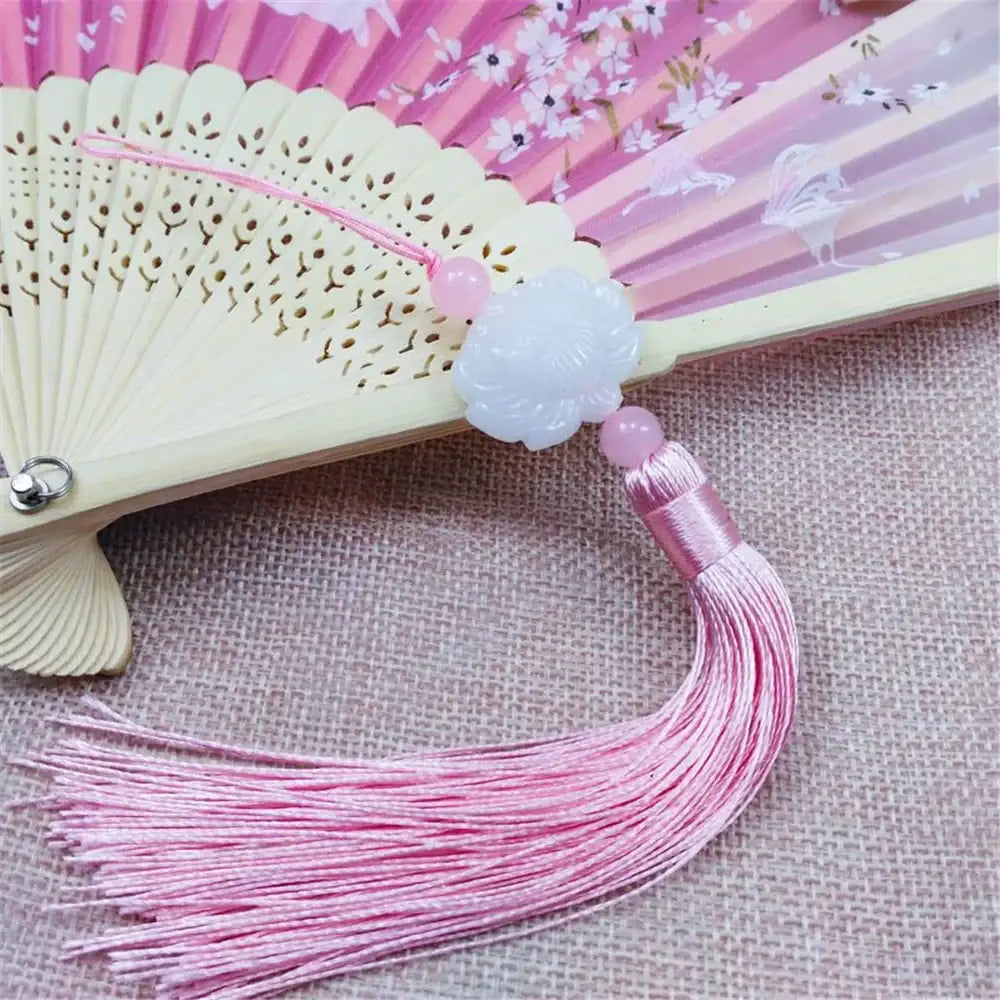 A delicate pink tassel charm with a carved white jade lotus pendant attached to a traditional folding fan for decor