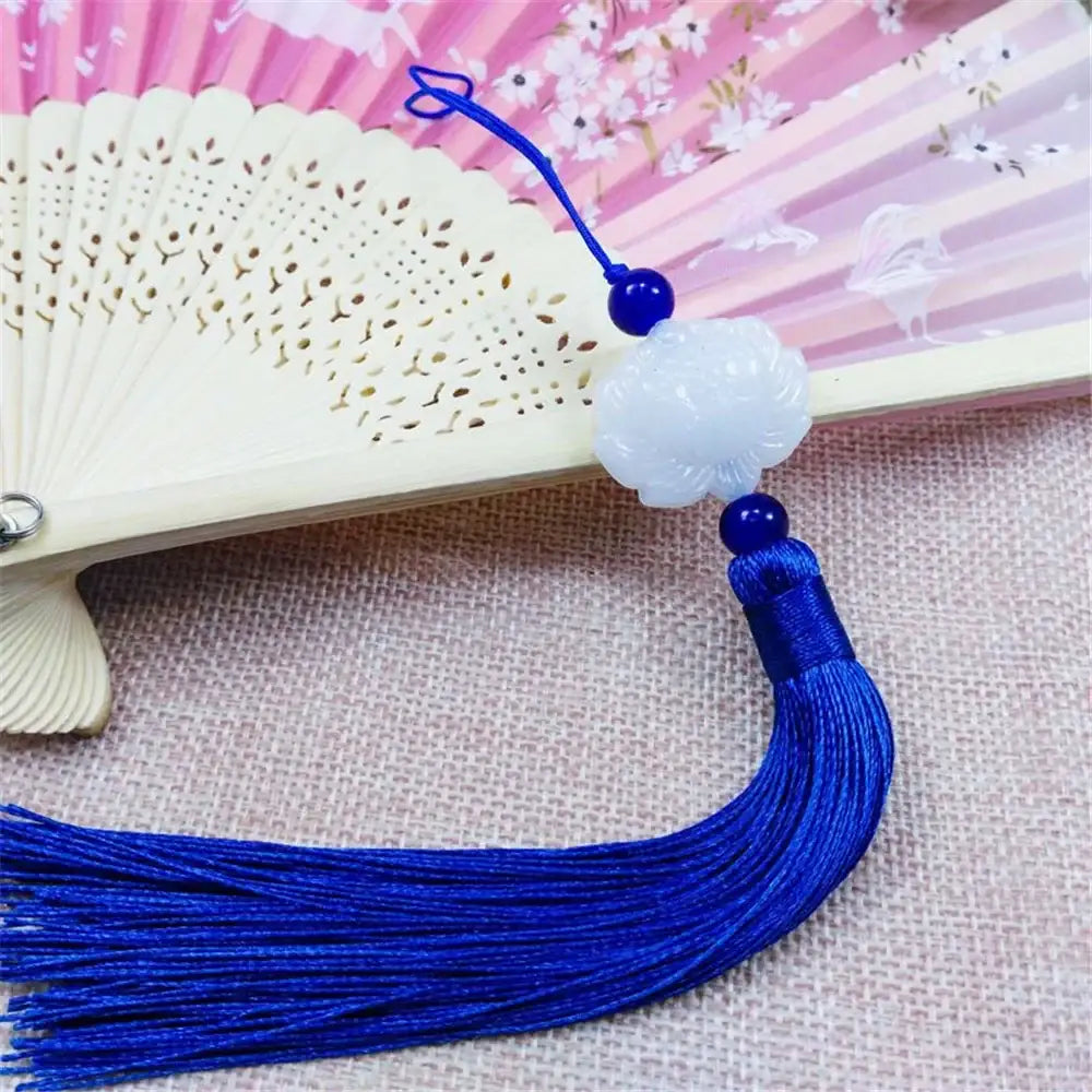 White jade lotus flower pendant with royal blue silk tassel and beads attached to an ornate fan for living room decor