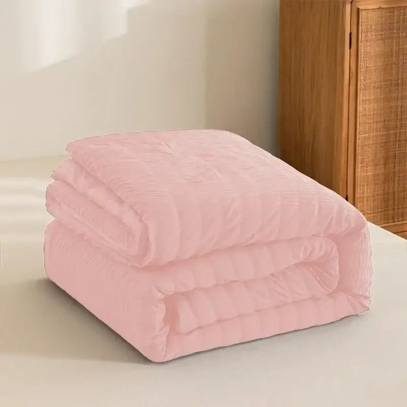 A soft pastel pink king size seersucker quilt with plush texture and subtle stitching patterns for all season use