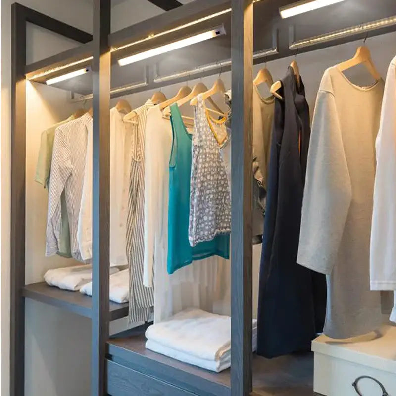 Modern gray wood-framed walk-in closet with white led motion sensor cabinet light illuminating neatly arranged clothing
