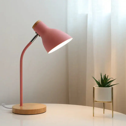 Pink macaron metal table light with adjustable gooseneck, curved metal arm, and wooden base for bedroom use