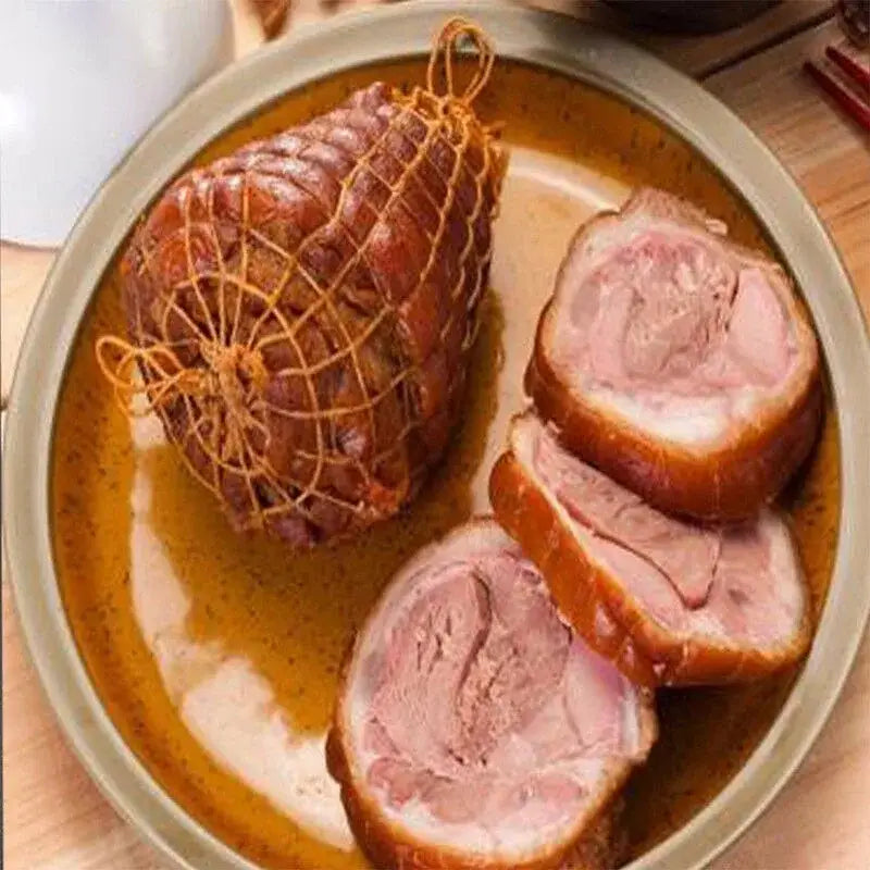 A glossy golden-brown roasted pork leg tied with white mesh bbq net from a bbq net bundle on a ceramic plate