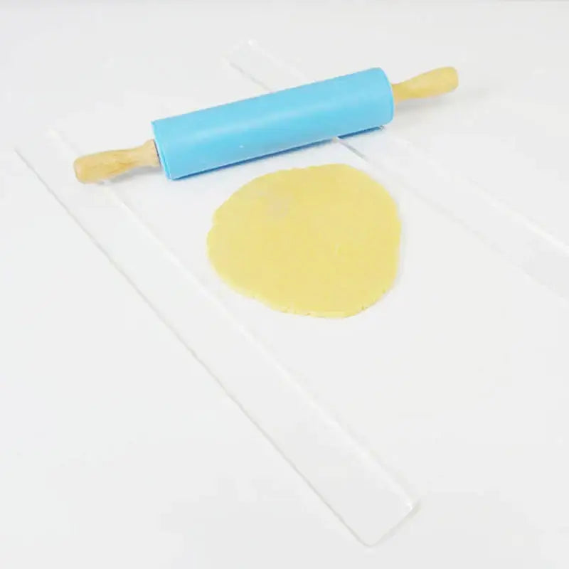 Blue plastic cake rolling tool with wooden handles beside flattened yellow dough on clear mat for biscuit cake rolling decorbites