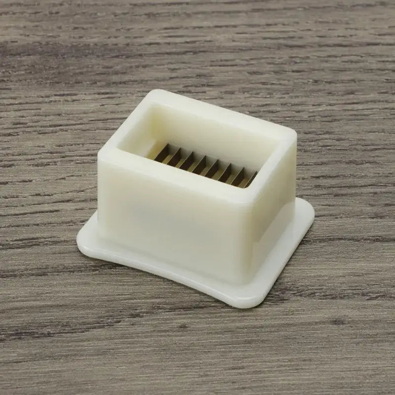 White plastic green bean slicer with square base and internal metal blades for efficient vegetable shredding