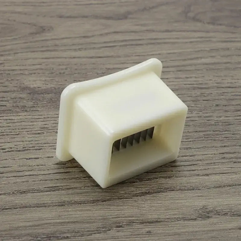 Off-white plastic green bean slicer with rectangular body and five metal tines for efficient bean shredding