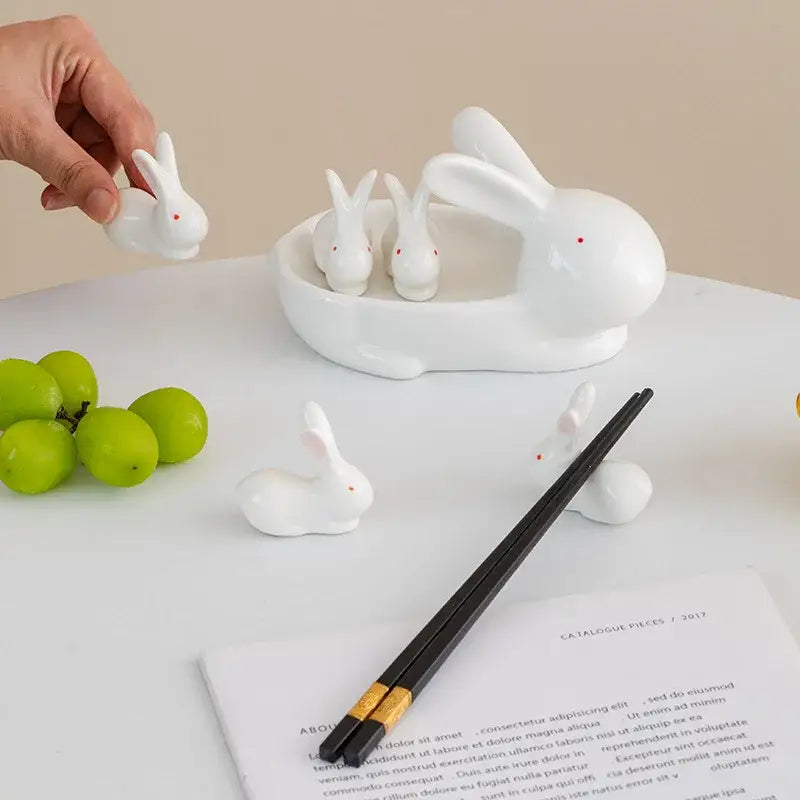 White ceramic rabbit figurine with red dot eyes held by hand alongside a white porcelain duck chopstick holder tray