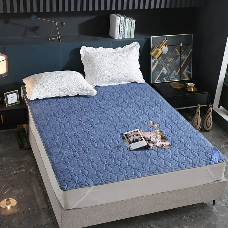 Blue quilted bed protector pad with diamond pattern paired with white pillowcases for bedroom use