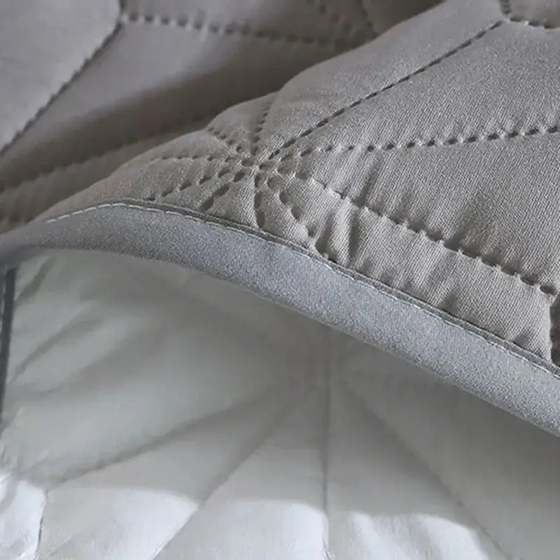 Gray quilted bed protector pad with soft textured surface and subtle stitching patterns for bedroom use