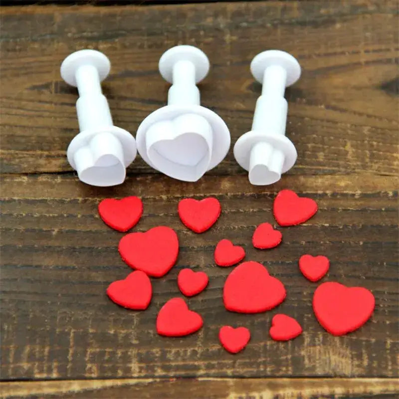 White plastic heart star cake decorating cookie cutters with matching red fondant hearts on a wooden surface