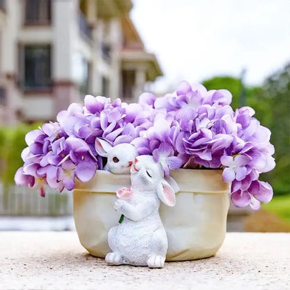 A white resin decorbites bunny succulent planter pot with pink accents beside a cream ceramic pot of purple hydrangeas