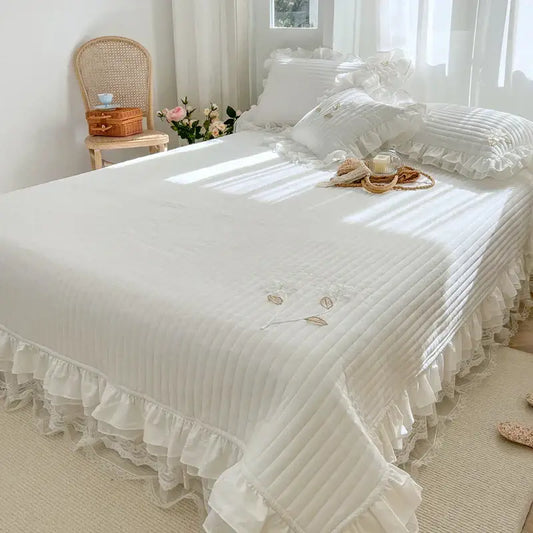 White quilted bedspread coverlet with delicate ruffled edges and embroidered leaf details for bedroom use