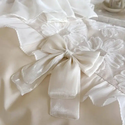 A delicate ivory satin bow with a subtle sheen on white french lace ruffles in a decorbites bedding set
