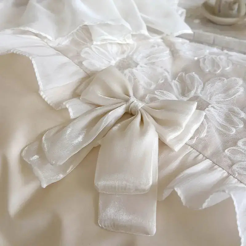 A delicate ivory satin bow with a subtle sheen on white french lace ruffles in a decorbites bedding set