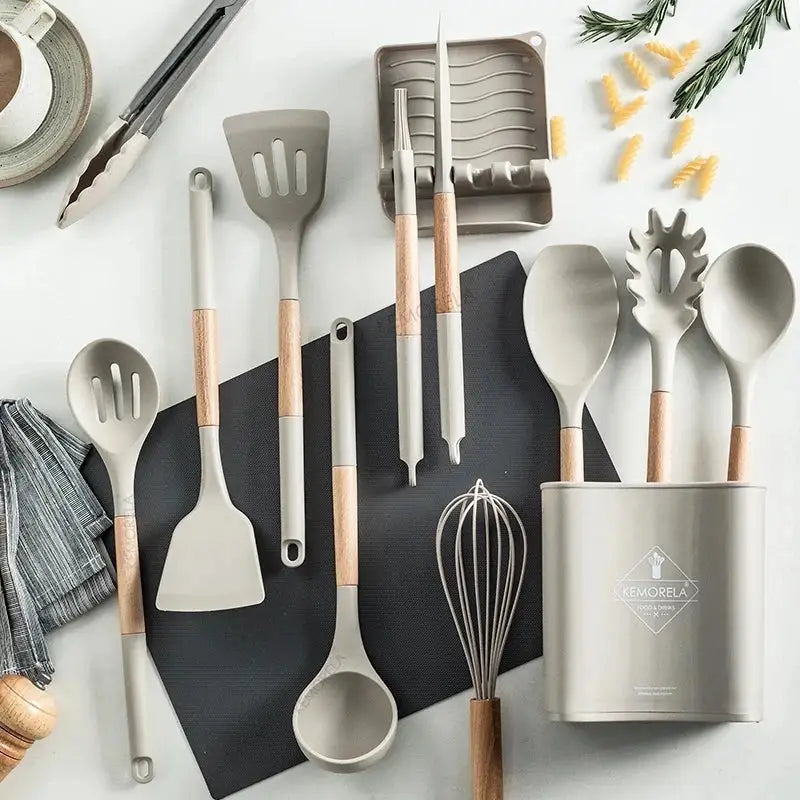 Set of gray silicone kitchen cookware utensils with wooden handles and matching holder on black mat cookware set