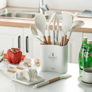 White silicone kitchen cookware set with wooden handles in a white ceramic utensil holder for kitchen organization