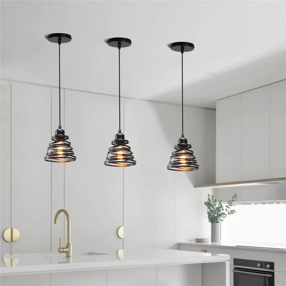 Three black decorbites iron cage pendant lights with spiral iron cage ring shades hang above a modern kitchen island