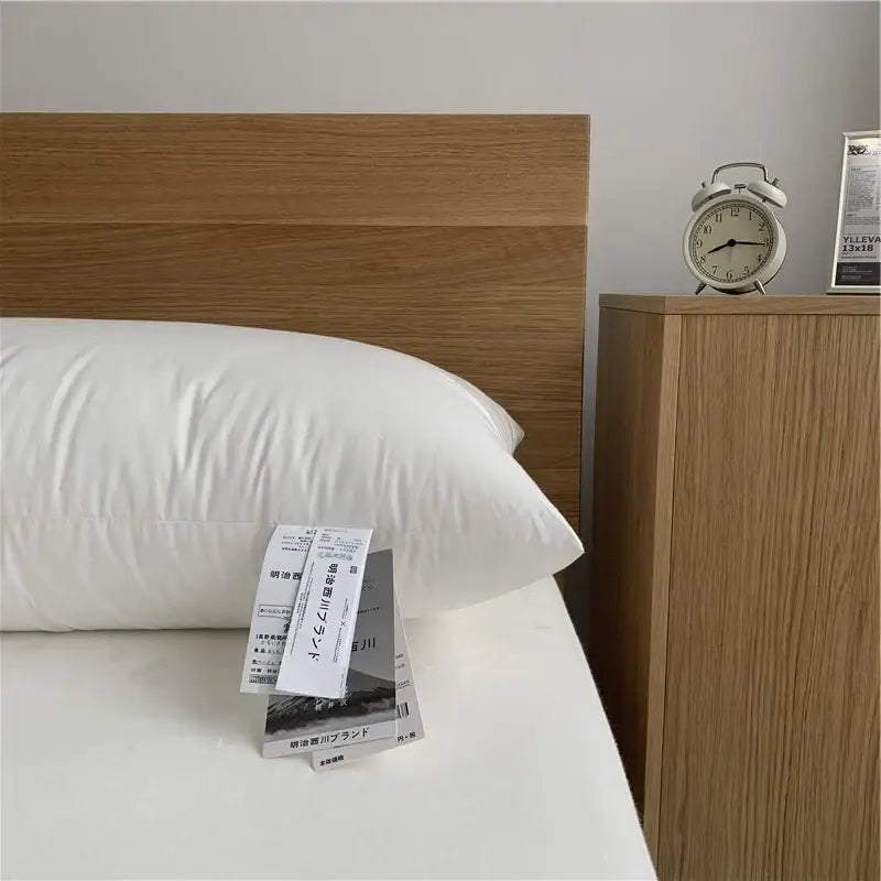 White textured cotton rectangle neck pillow with subtle texture resting on bed beside wooden headboard