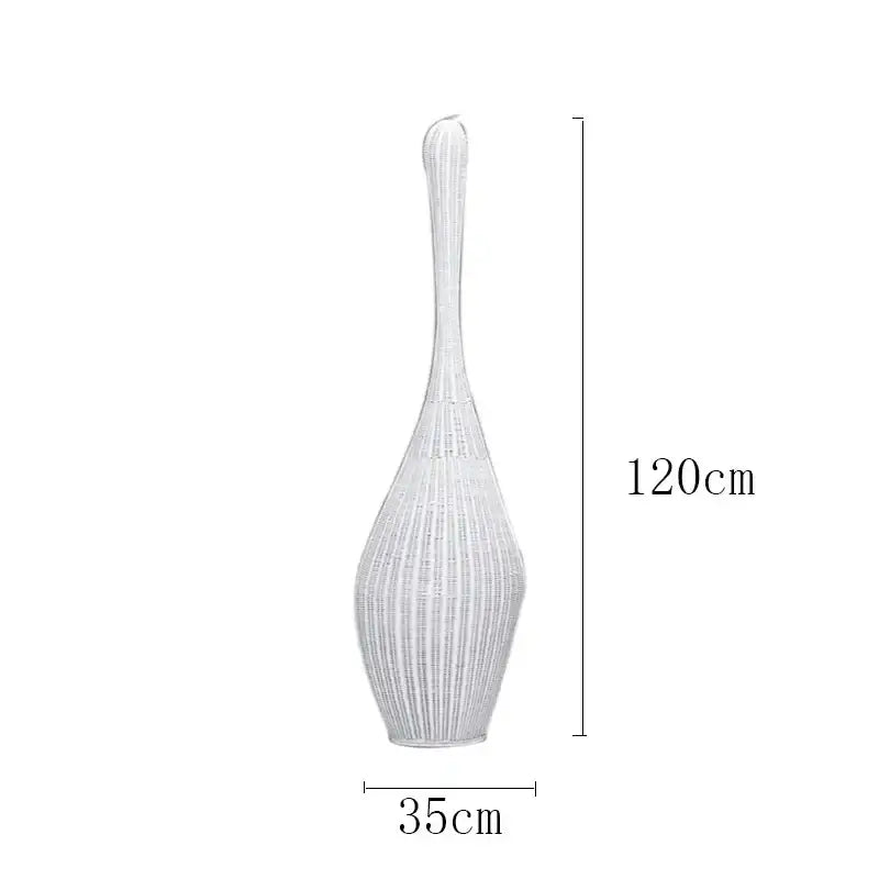 A tall slender white woven vase with flared top and tapered base next to a wicker dark brown bamboo floor lamp decorbites
