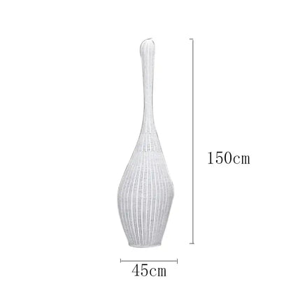 A tall slender white woven vase with a flared top complementing decorbites bamboo floor lamp for warm living room light