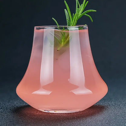 A sleek decorbites crystal whiskey glass tumbler with flared base holds a pink cocktail garnished with fresh rosemary