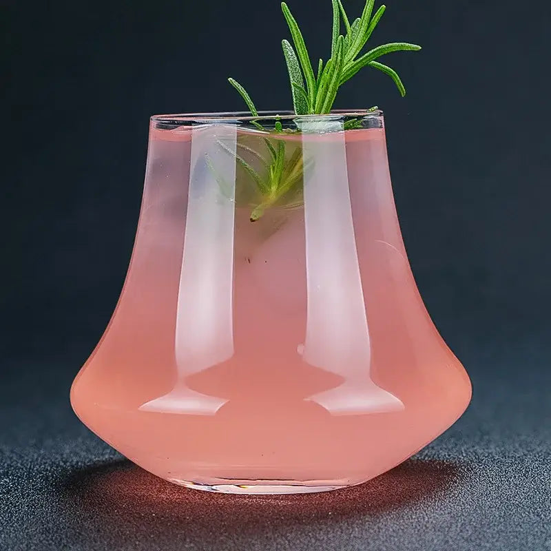A sleek decorbites crystal whiskey glass tumbler with flared base holds a pink cocktail garnished with fresh rosemary