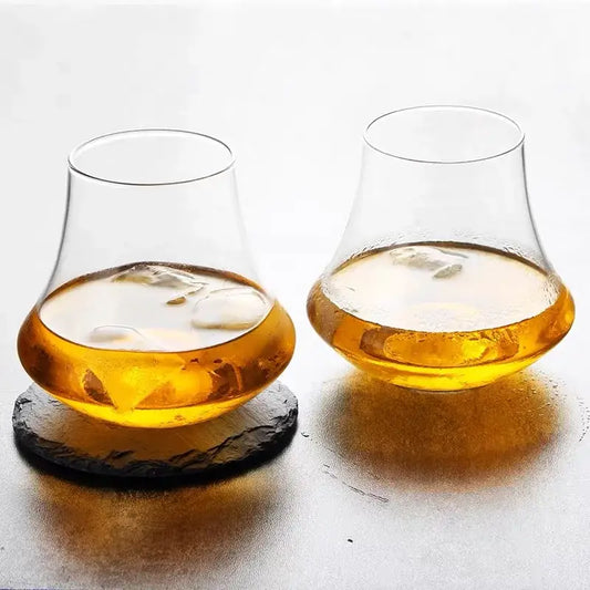 Two decorbites crystal whiskey glass tumblers with wide bowls filled with amber liquid and ice cubes for spirits