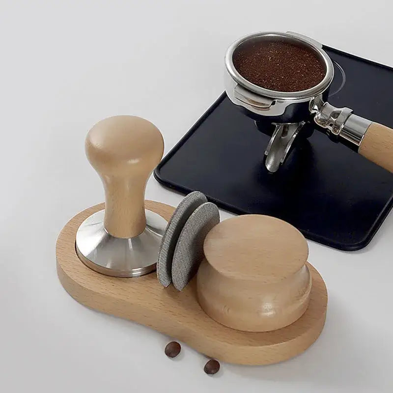 Light wood espresso distributor tamper with rounded handle and metallic base on wooden tray with two gray fabric tampers