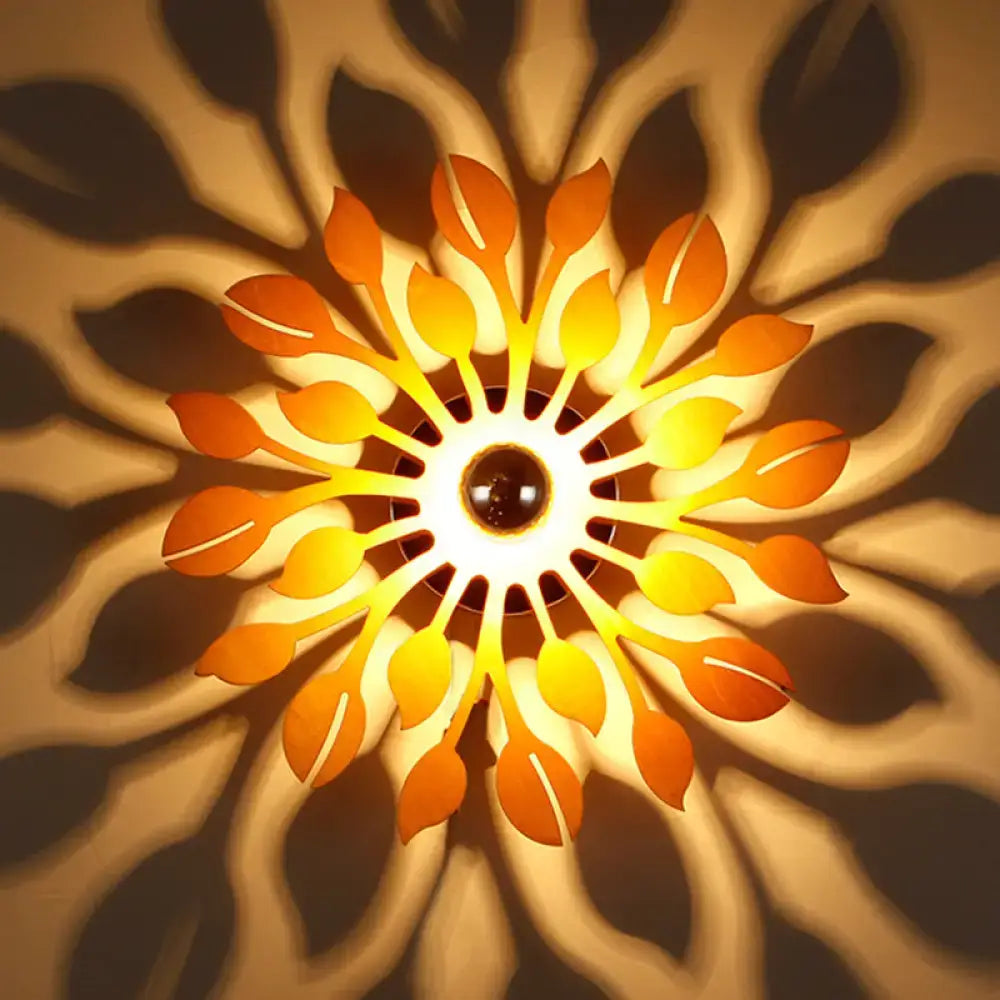 A warm glowing wooden floral sunburst wall lamp with orange and yellow leaf-shaped panels for bedroom lighting