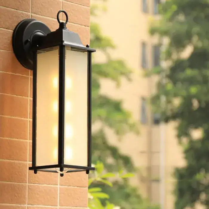 Black wrought iron wall lantern with frosted glass panels warm glowing light decorbites black finish outdoor porch light