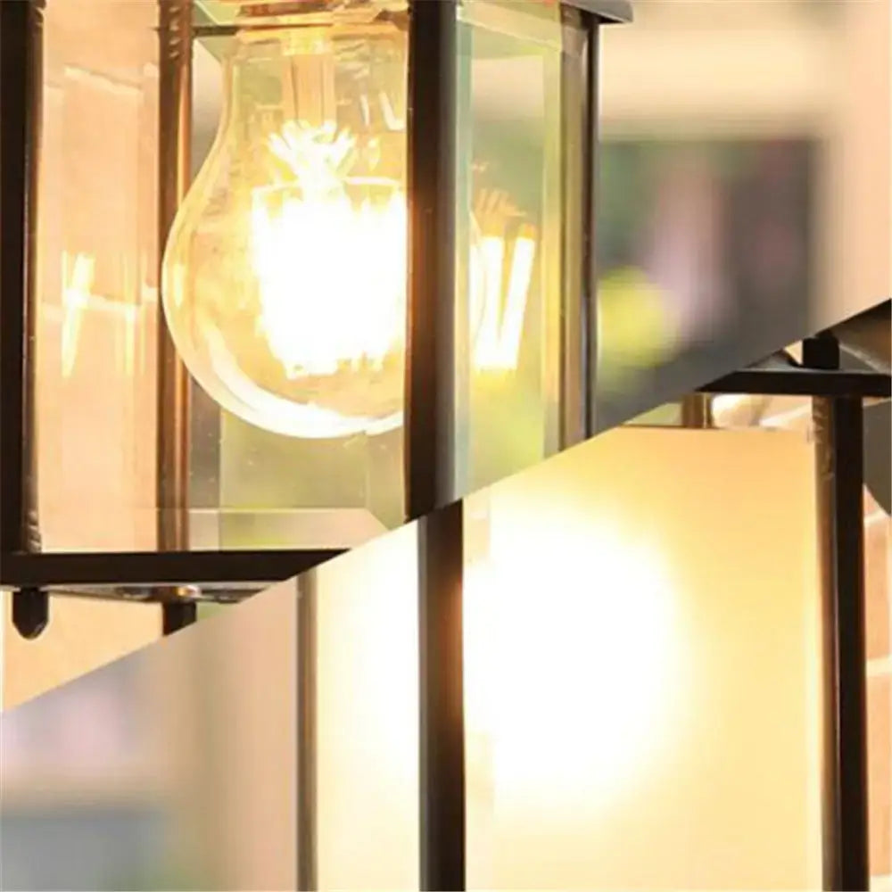 A warm glowing vintage-style wall lantern with black finish wrought iron frame and exposed filament bulb for outdoor use
