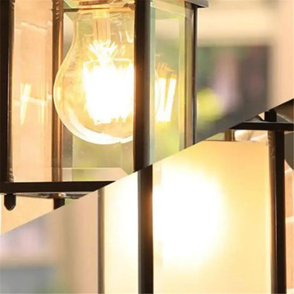 A warm glowing vintage-style wall lantern with black finish wrought iron frame and exposed filament bulb for outdoor use