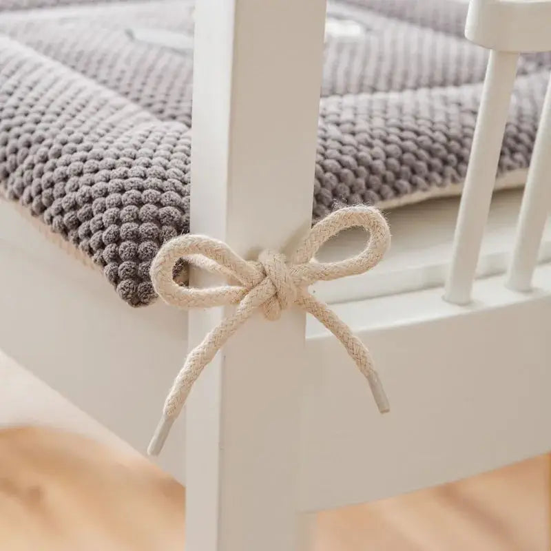 Cream-colored rope bow tied around white wooden chair leg of yellow and gray decorbites cartoon embroidered seat cushion