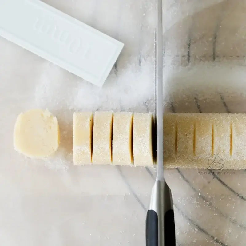 A pale yellow sugar coated dough log sliced with a kitchen knife using a yellow biscuit cake rolling mold with scale ruler for decorbites biscuit cake rolling
