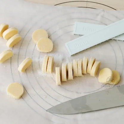 Sliced pale yellow decorbites biscuit cake dough beside blue silicone cookie cutters and chef knife using cake rolling mold