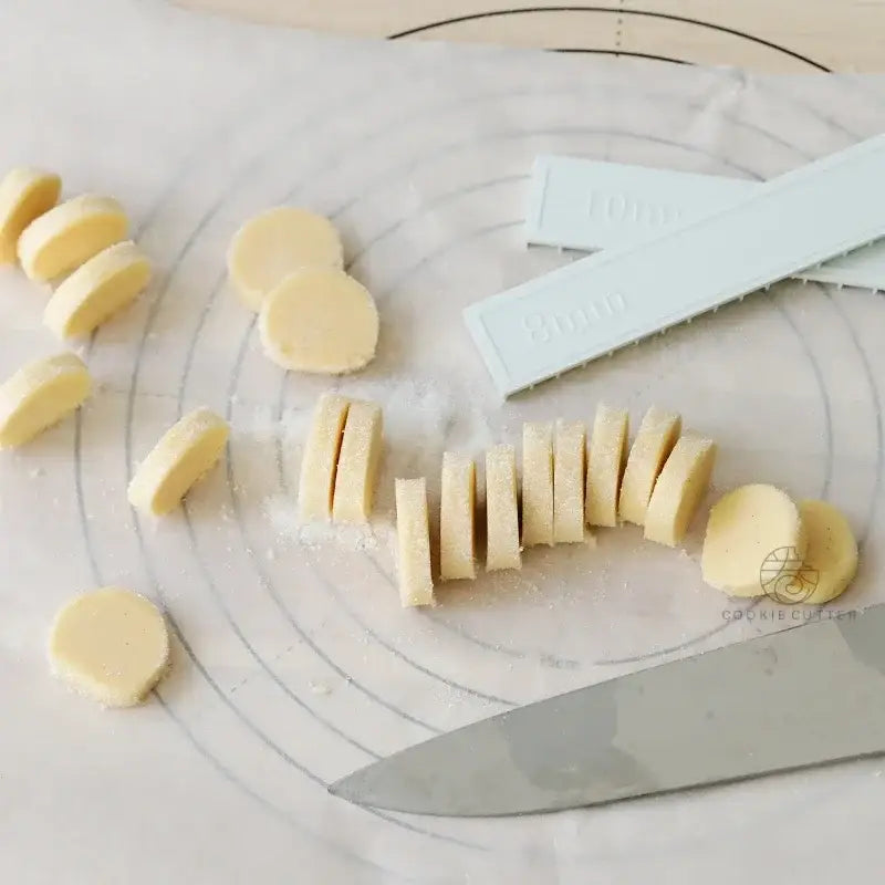 Sliced pale yellow decorbites biscuit cake dough beside blue silicone cookie cutters and chef knife using cake rolling mold