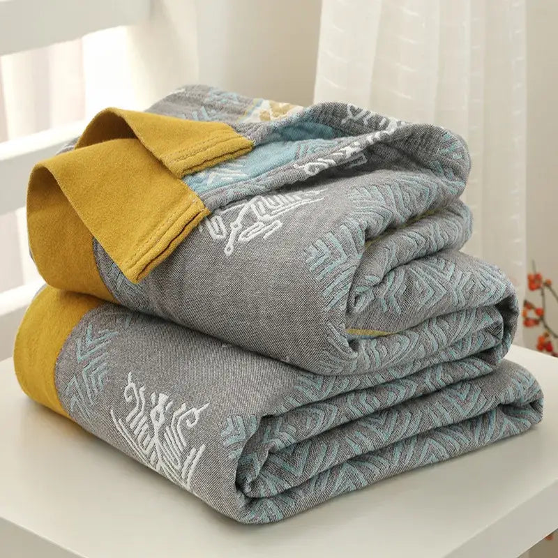 Stacked gray and mustard-yellow throw blankets with embroidered geometric patterns in cotton stripe gauze towel quilt style
