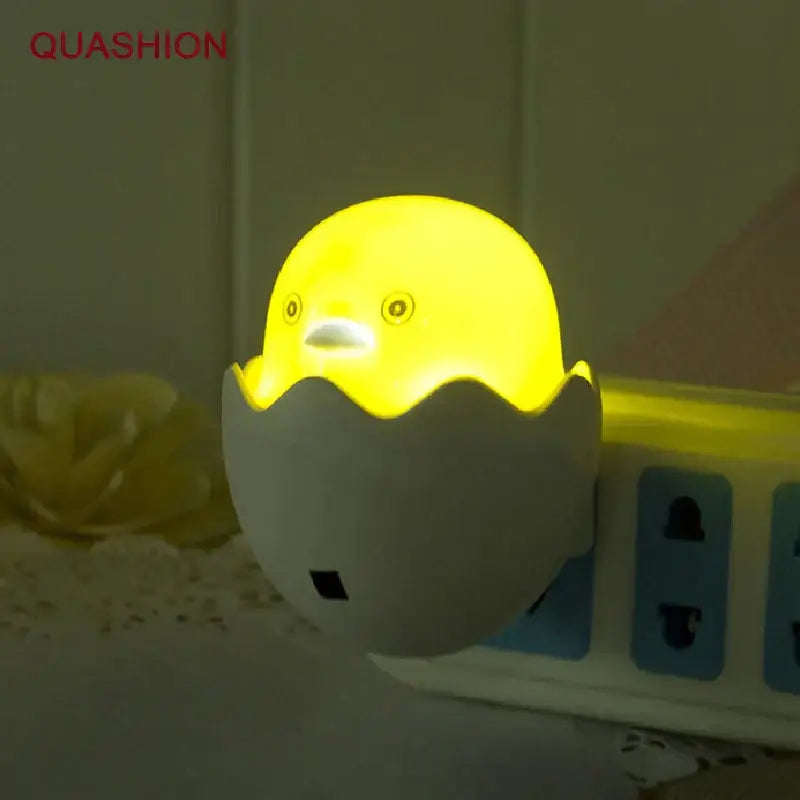 Yellow chick in eggshell led night light glowing softly plugged into a power strip for bedroom use with sensor lamp function