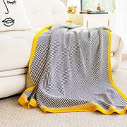A cozy decorbites knitted diagonal stripe sofa blanket with a black and white herringbone pattern and yellow edges
