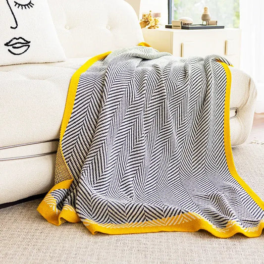A cozy decorbites knitted diagonal stripe sofa blanket with a black and white herringbone pattern and yellow edges